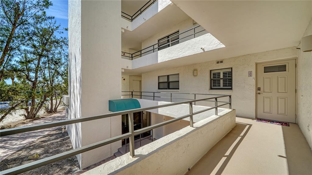 An exterior view of a multi-story apartment building with open-air walkways and a tan door — 8735 MIDNIGHT PASS ROAD UNIT 105B, SARASOTA, FL