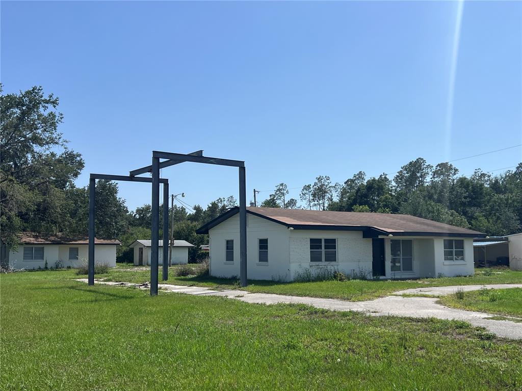 A white single-story house features a large metal frame structure standing in the front yard — 34020 & 34024 STATE ROAD 54, WESLEY CHAPEL, FL