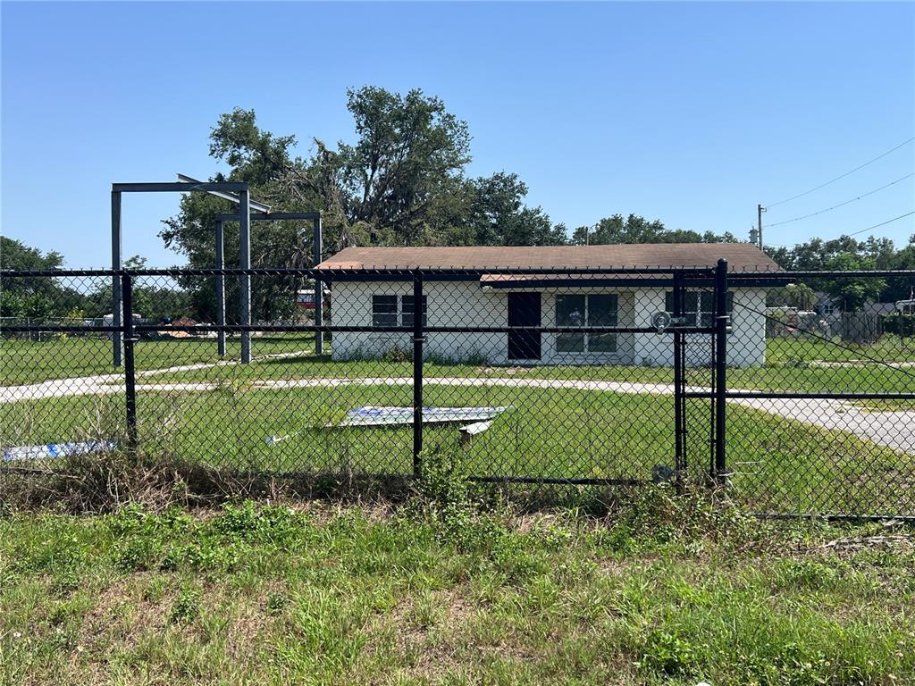 A single-story white house sits behind a chain-link fence with a metal frame structure nearby — 34020 & 34024 STATE ROAD 54, WESLEY CHAPEL, FL
