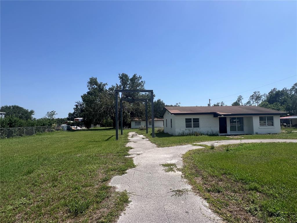 A single-story white house with a metal pergola structure over a cracked concrete walkway — 34020 & 34024 STATE ROAD 54, WESLEY CHAPEL, FL