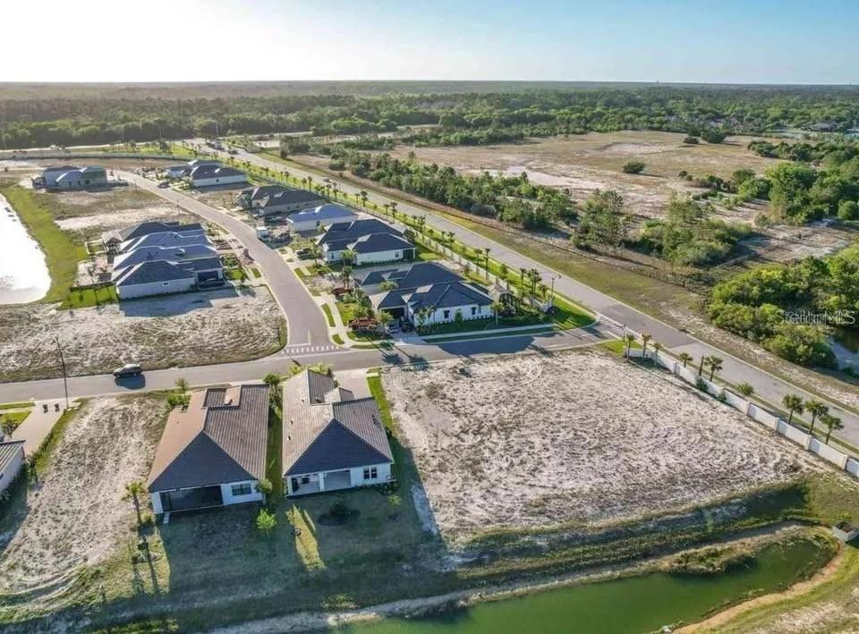 An aerial view shows several suburban houses and a vacant lot near a small pond — 87 DEL PALMA DRIVE, PALM COAST, FL