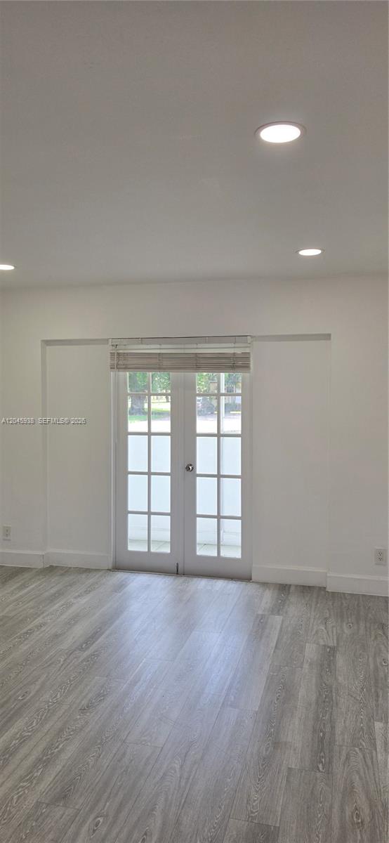 A room with white walls, recessed lighting, and light-colored wood-look flooring features double glass doors — AVENTURA, FL