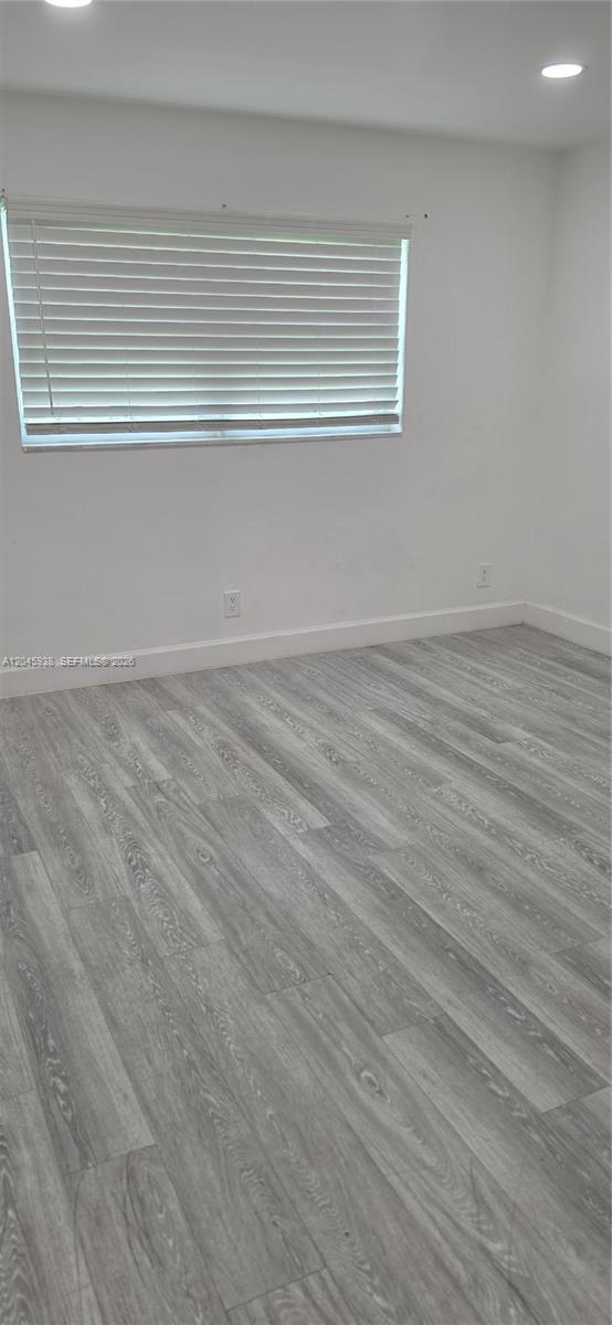An empty room features white walls, light-colored wood-look flooring, and a window with white blinds — AVENTURA, FL