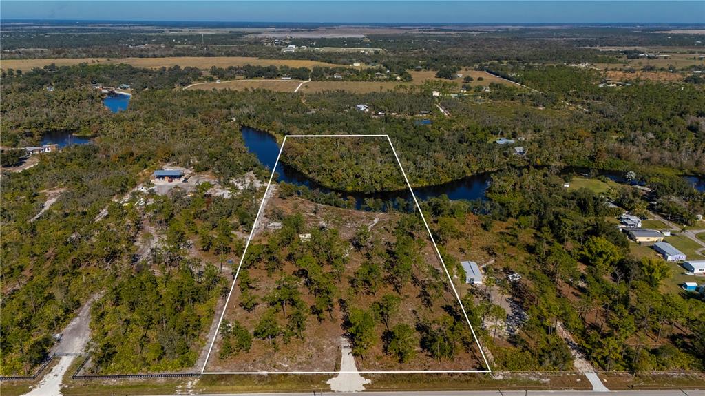 An aerial view shows a vacant, wooded lot with a river bordering the rear boundary — 36051 WASHINGTON LOOP ROAD, PUNTA GORDA, FL