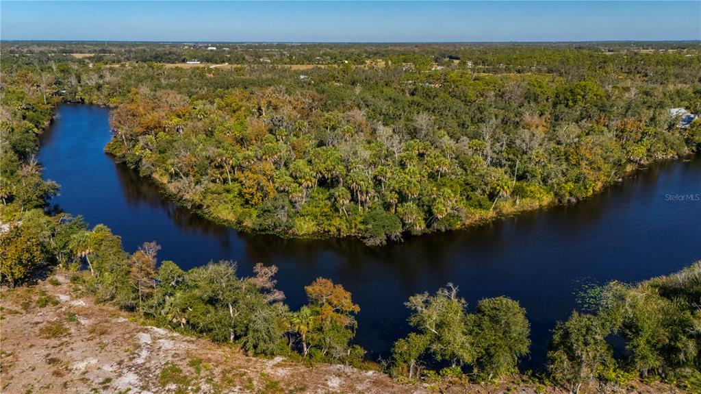 An aerial view shows a winding river bordered by dense trees and a sandy bank — 36051 WASHINGTON LOOP ROAD, PUNTA GORDA, FL
