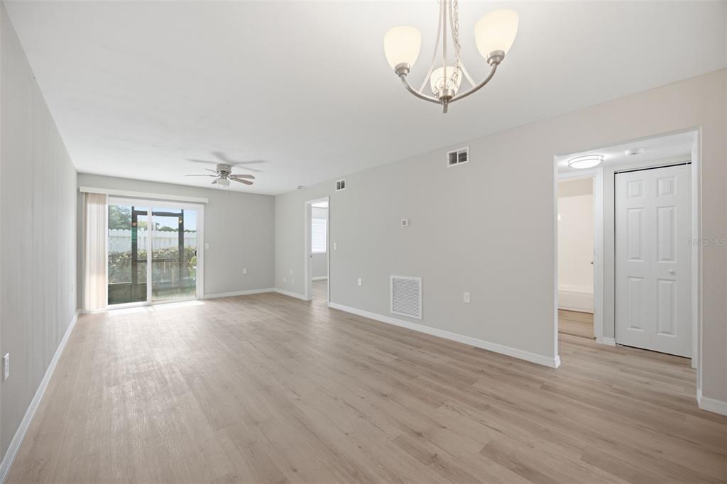 A bright living room features light wood-look flooring, a ceiling fan, and a sliding glass door — 39132 COUNTY ROAD 54 UNIT 2018, ZEPHYRHILLS, FL