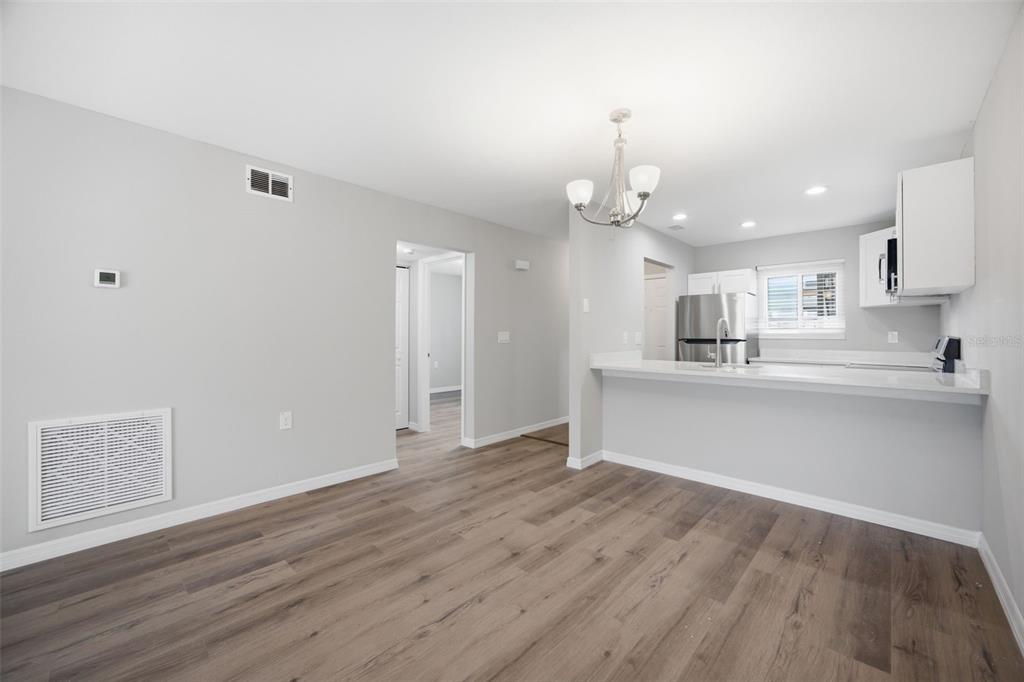 A living area with wood-look flooring opens to a kitchen featuring a breakfast bar — 39132 COUNTY ROAD 54 UNIT 2018, ZEPHYRHILLS, FL