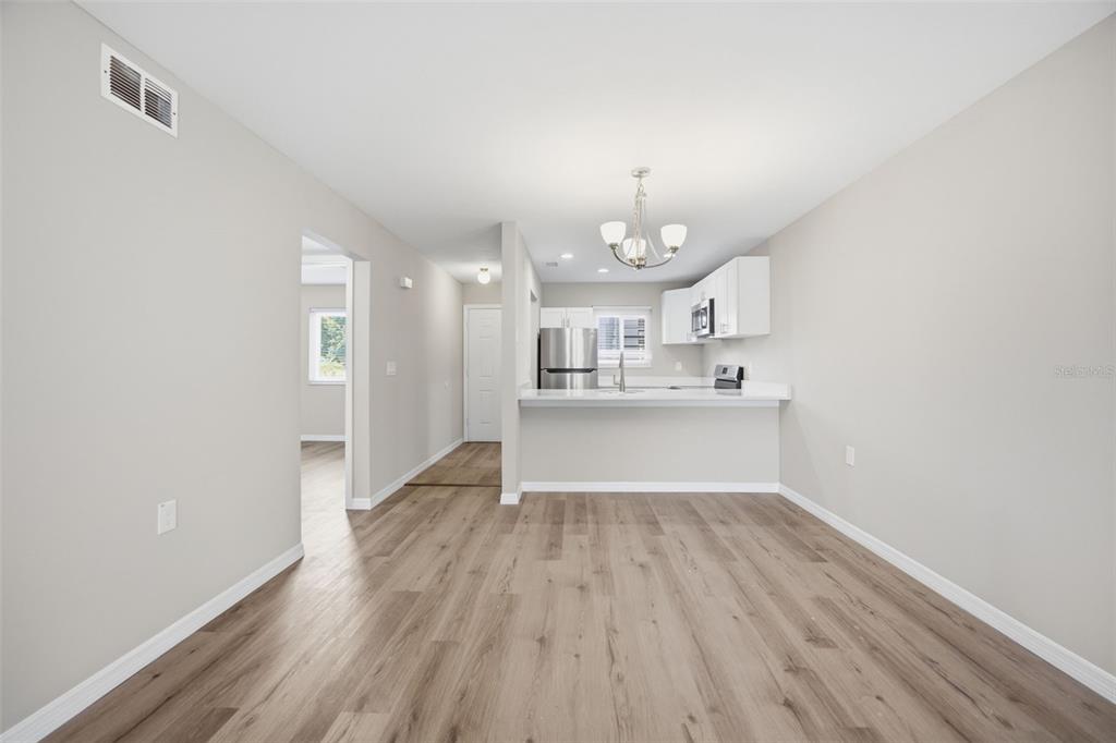 An open-concept dining area leads to a kitchen with white cabinets and wood-look flooring — 39132 COUNTY ROAD 54 UNIT 2018, ZEPHYRHILLS, FL