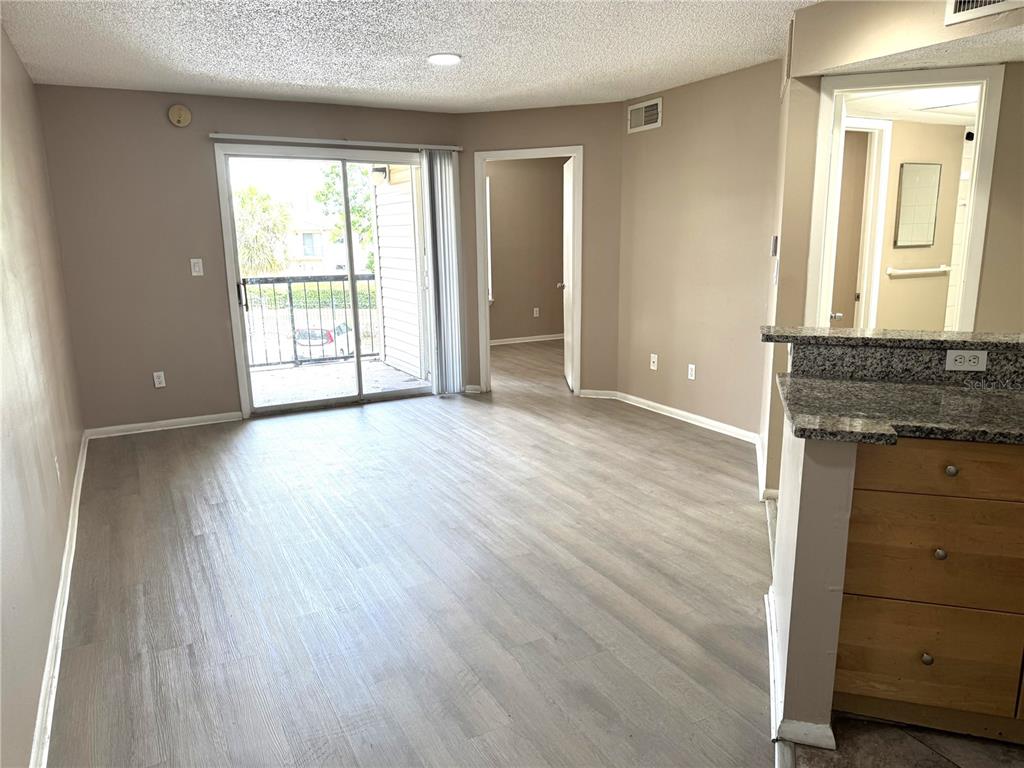 A living room with light wood-look flooring, a sliding glass door, and an adjacent kitchen — 1916 LAKE ATRIUMS CIRCLE UNIT 32, ORLANDO, FL