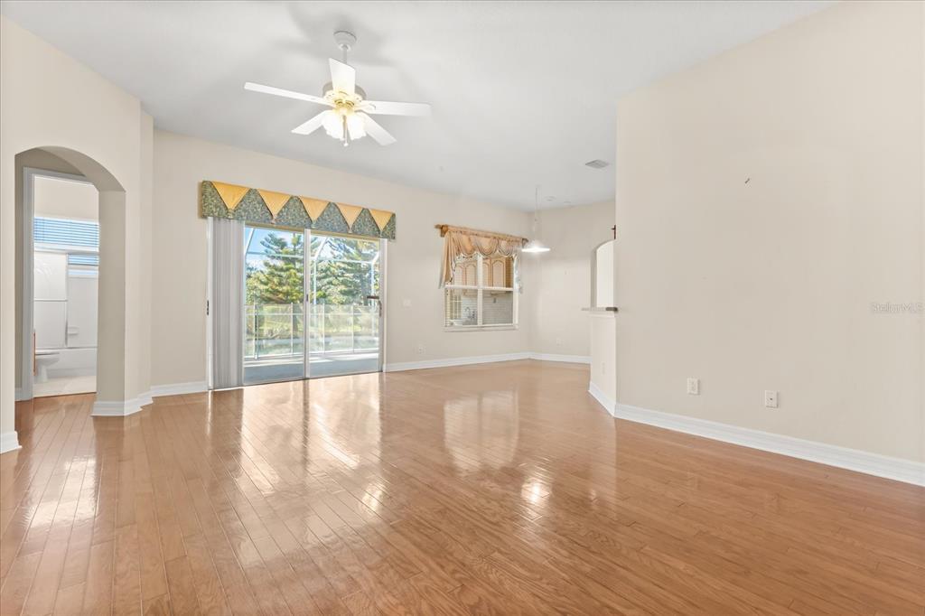 An empty living room features hardwood floors, a ceiling fan, and sliding glass patio doors — 19027 DOVE CREEK DRIVE, TAMPA, FL