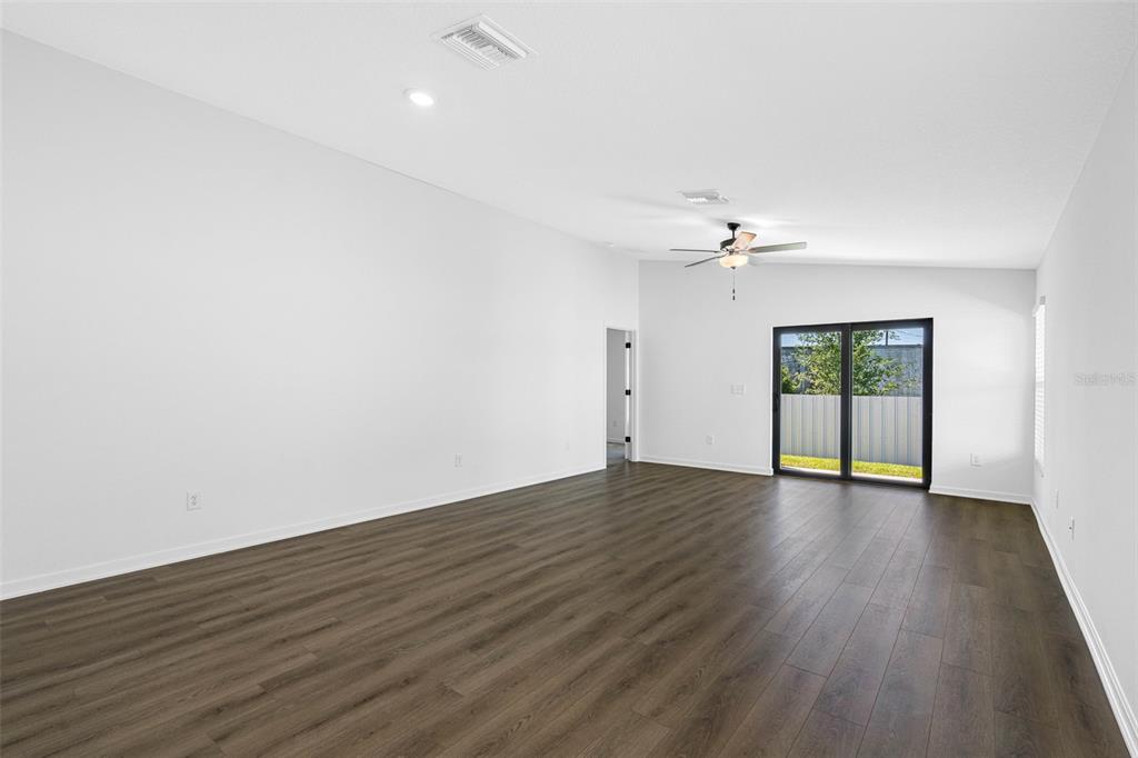 A spacious room with white walls, dark wood-look flooring, a ceiling fan, and sliding glass doors — 5335 CAP ROAD, BROOKSVILLE, FL