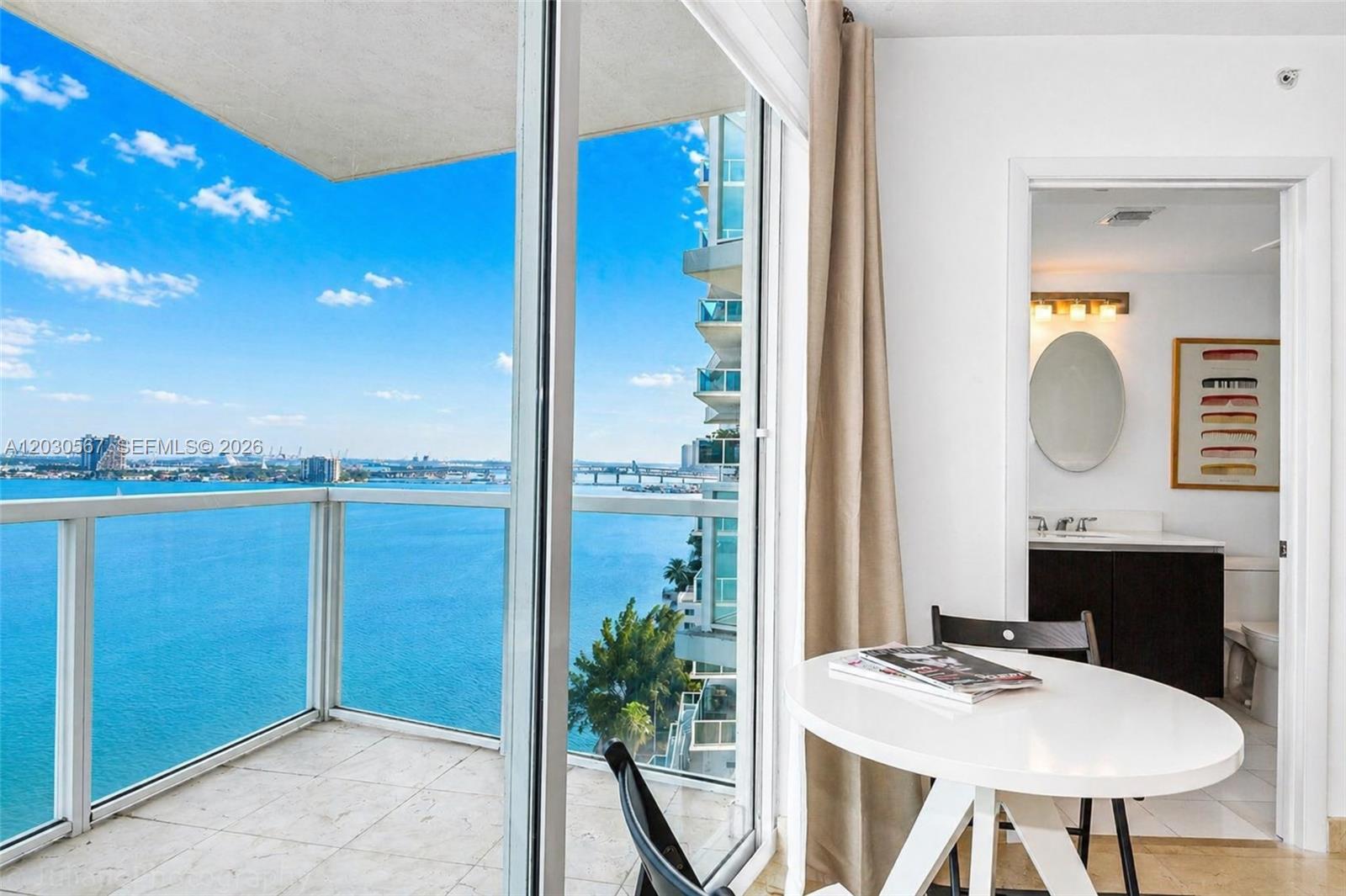 A white table sits near a balcony overlooking the ocean and a neighboring building — 665 NE 25th St # 1202, Miami FL 33137, MIAMI, FL