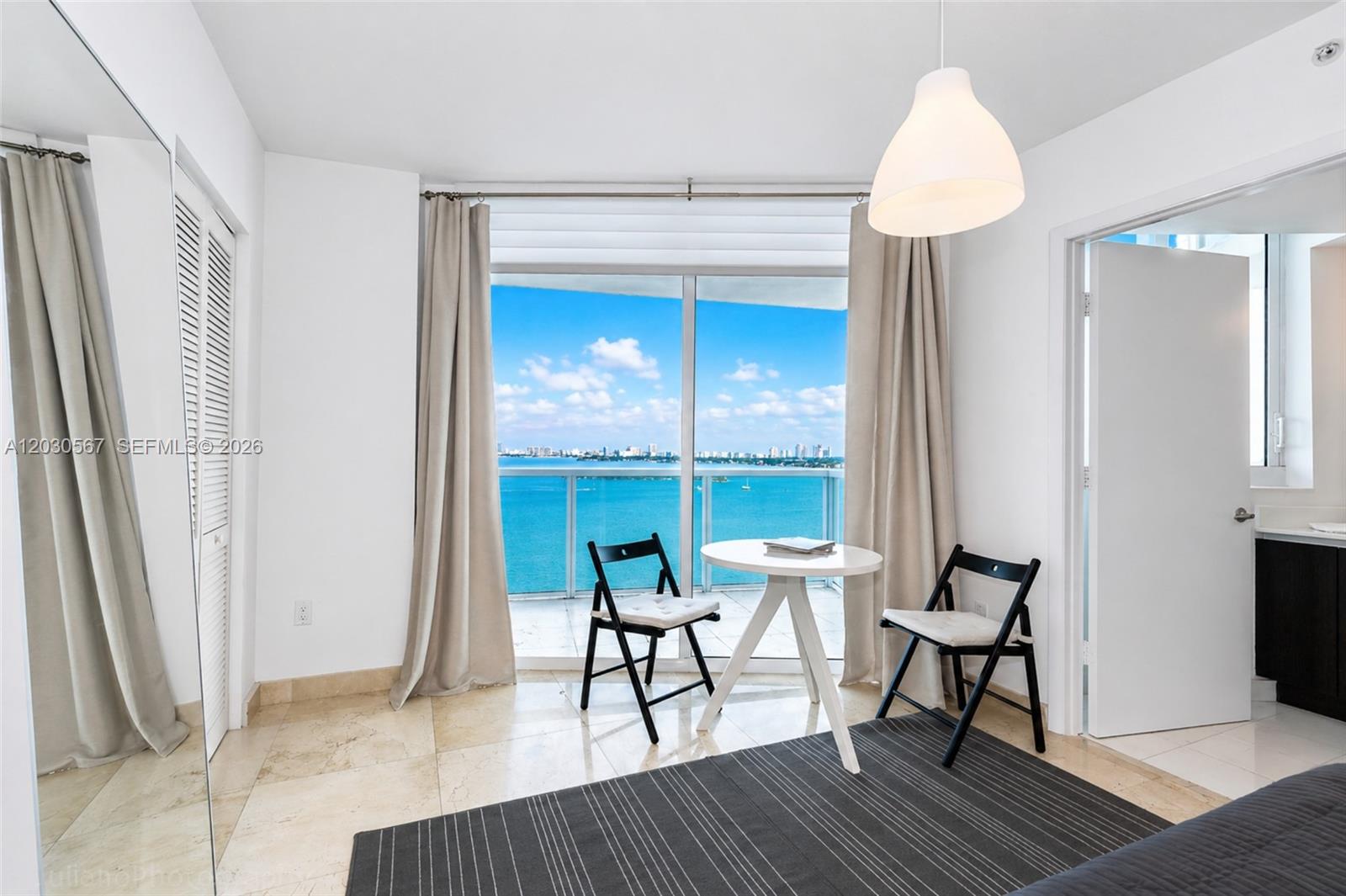 A bedroom features a small dining set, a large window with a water view, and tile floors — 665 NE 25th St # 1202, Miami FL 33137, MIAMI, FL