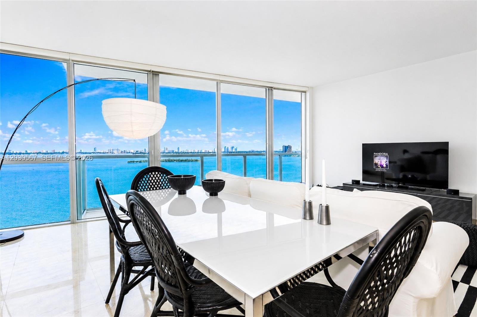 A dining area with a white table and black chairs overlooks a bay and city skyline — 665 NE 25th St # 1202, Miami FL 33137, MIAMI, FL