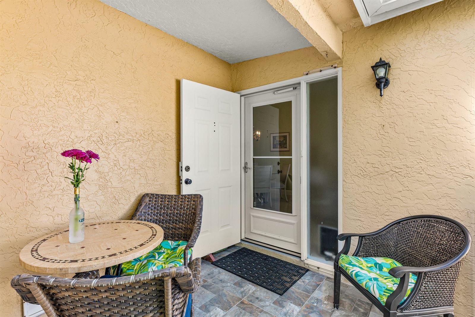 A small patio features a round stone table, two wicker chairs, and a glass-paneled door — 501 Waterside Drive, Hypoluxo FL 33462, HYPOLUXO, FL