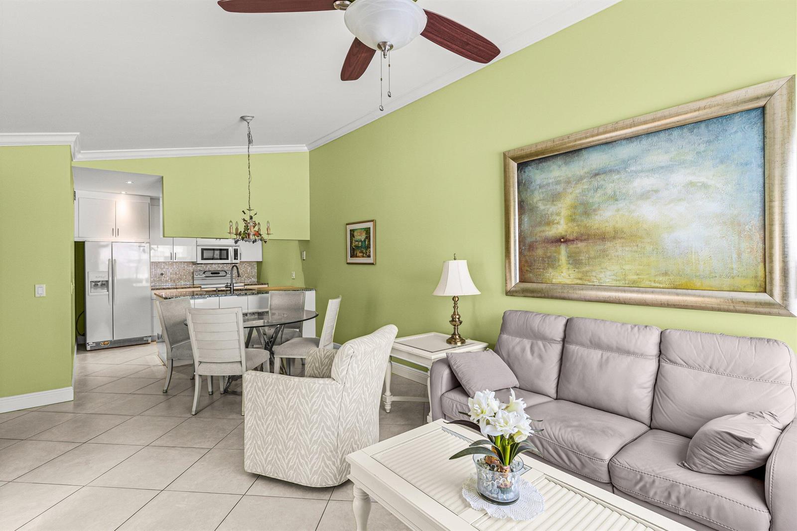 A living room and dining area with light green walls, tile flooring, and a grey sofa — 501 Waterside Drive, Hypoluxo FL 33462, HYPOLUXO, FL