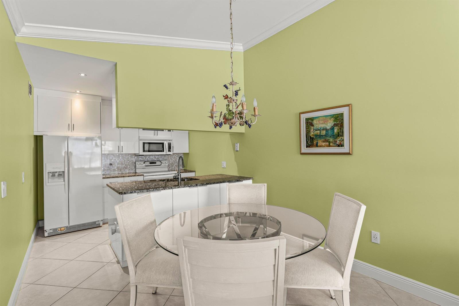 A dining area with a glass table and chairs sits adjacent to a white kitchen — 501 Waterside Drive, Hypoluxo FL 33462, HYPOLUXO, FL