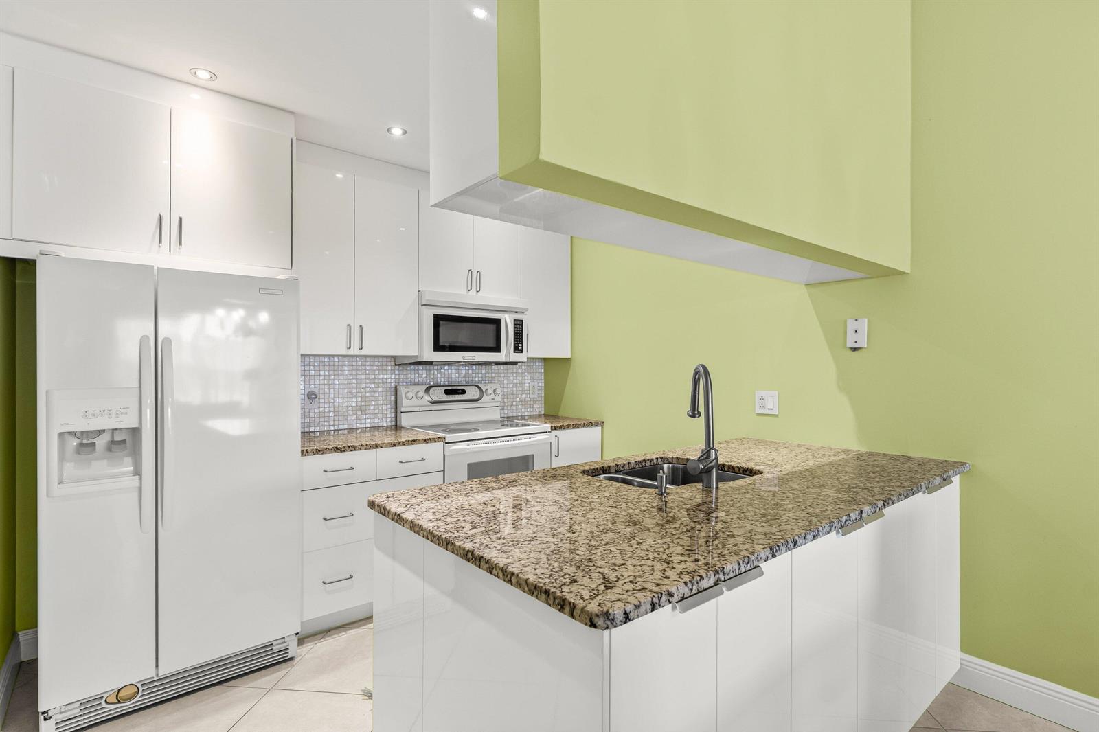 A kitchen features white cabinetry, granite countertops, a central island with a sink, and lime-green walls — 501 Waterside Drive, Hypoluxo FL 33462, HYPOLUXO, FL