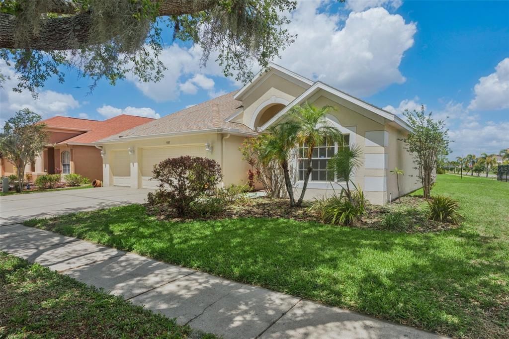 A single-story house with a beige stucco exterior, a two-car garage, and a front lawn — 9103 PINEBREEZE DRIVE, RIVERVIEW, FL