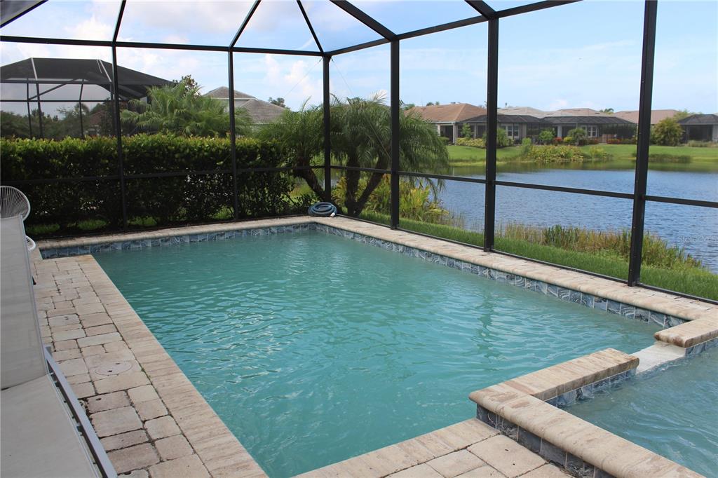 A screened-in swimming pool and spa overlooking a lake with neighboring houses in the background — 5826 LONG SHORE LOOP, SARASOTA, FL