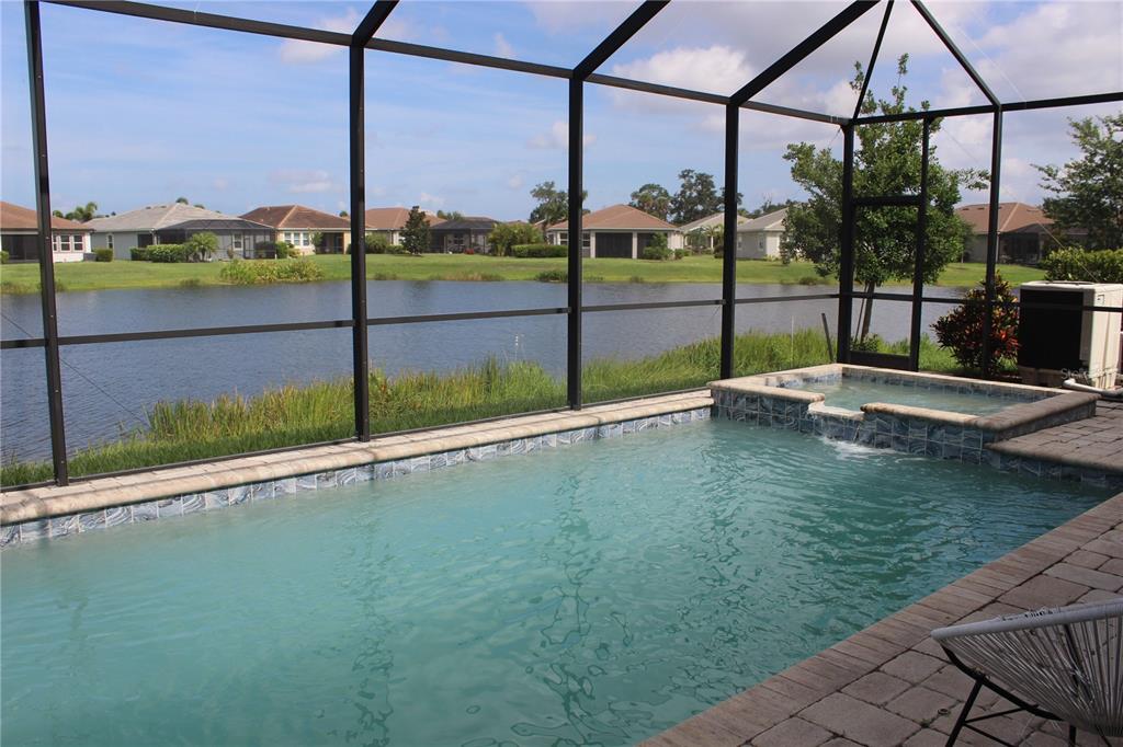 A screened-in pool and spa overlook a lake behind a row of suburban houses — 5826 LONG SHORE LOOP, SARASOTA, FL