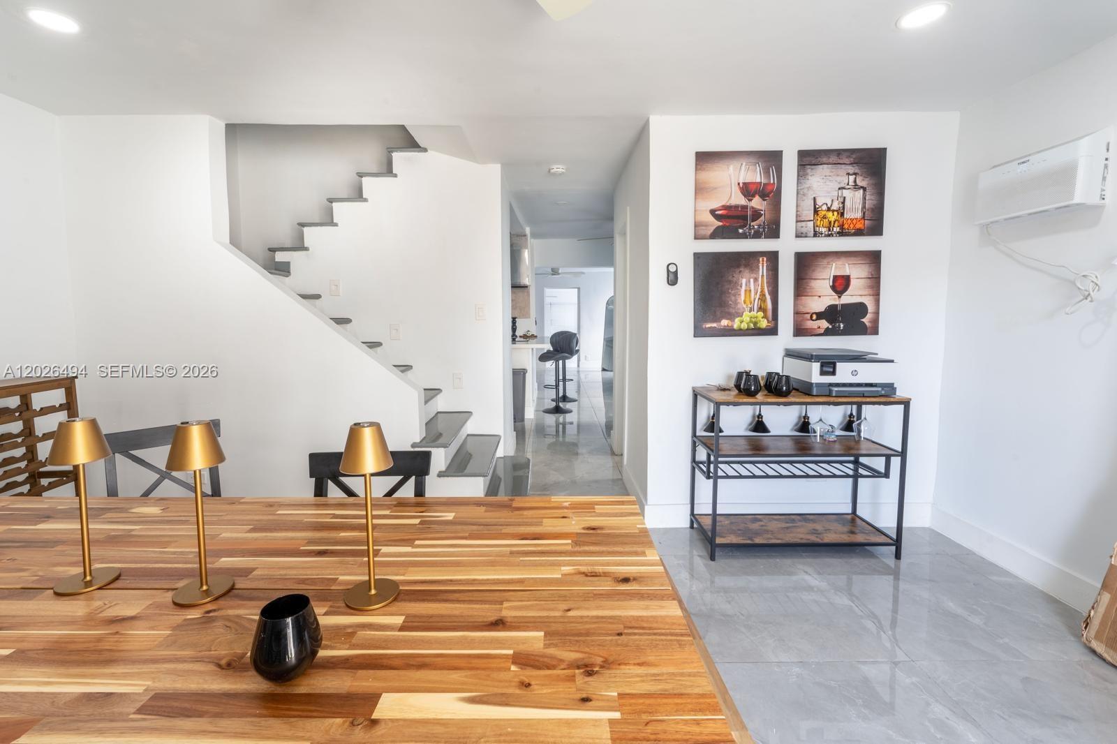 A dining area features a wooden table, a staircase, and a bar cart with wall art — 711 85th St, Miami Beach FL 33141, MIAMI BEACH, FL