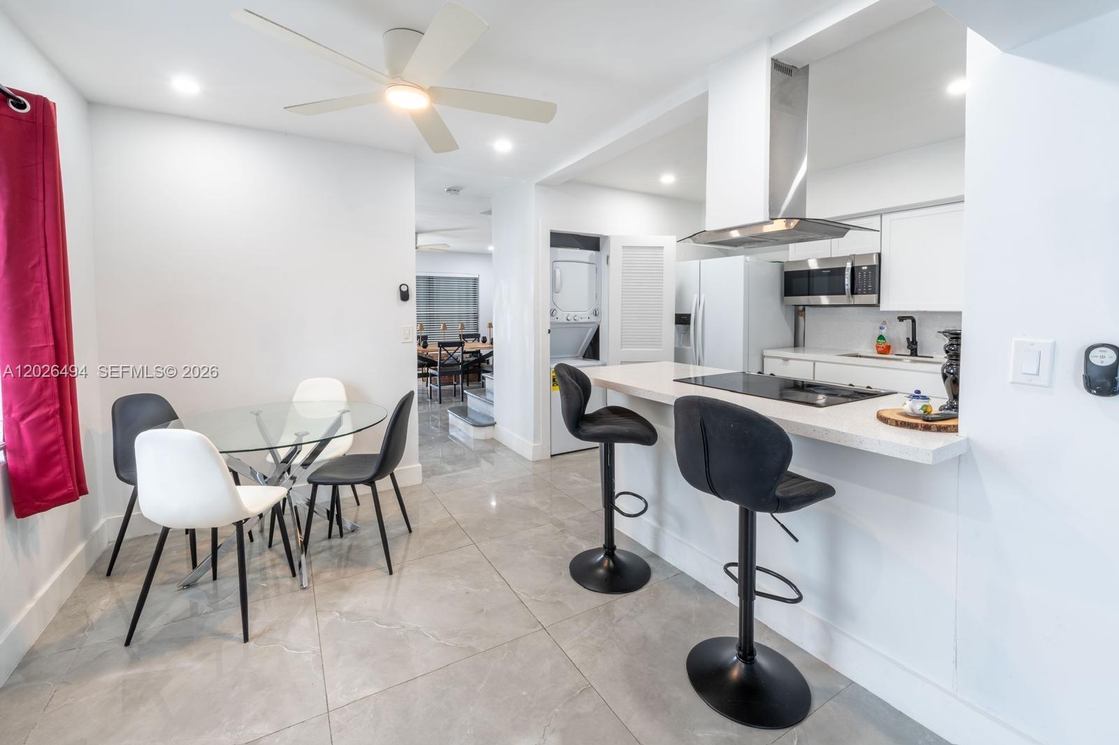 A modern kitchen and dining area feature white cabinetry, a breakfast bar, and tiled floors — 711 85th St, Miami Beach FL 33141, MIAMI BEACH, FL