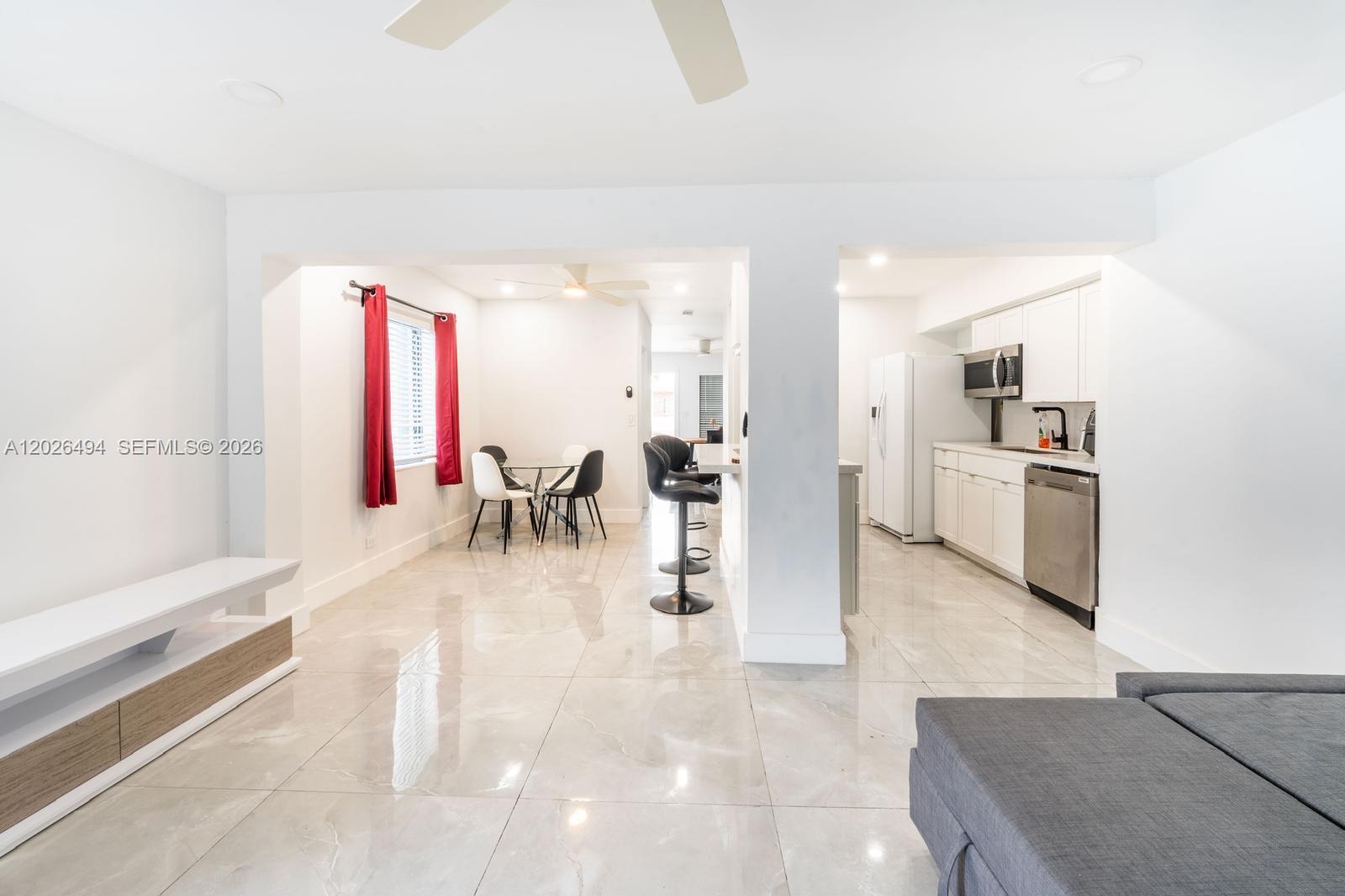 An open-concept living area features white cabinetry, a kitchen island, and glossy tile flooring — 711 85th St, Miami Beach FL 33141, MIAMI BEACH, FL