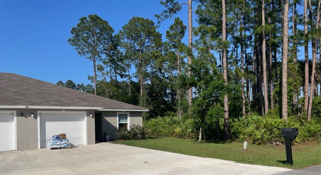 A single-story house with a two-car garage sits next to a wooded area — 33 PONDEROSA LANE, PALM COAST, FL