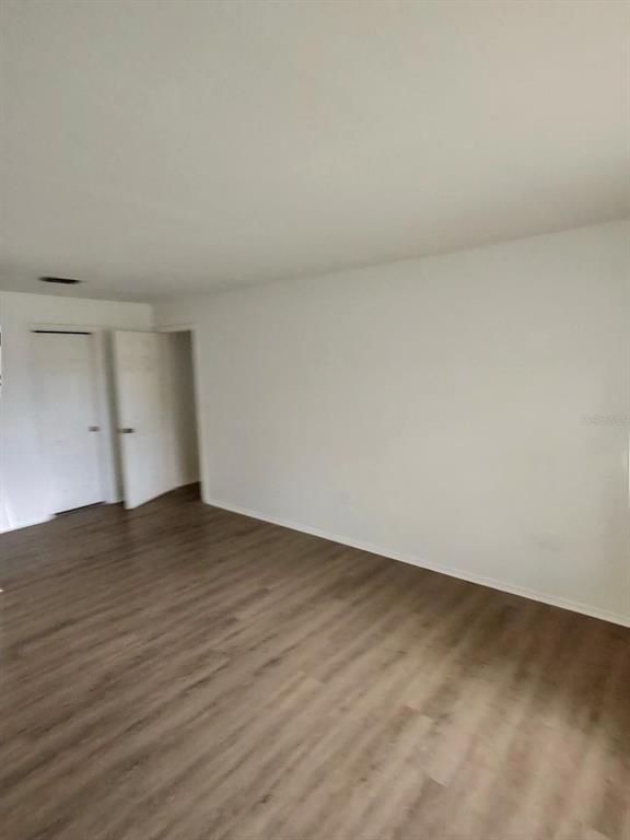 An empty room features light wood-look flooring and white walls with two open doorways — 6008 VILLAGE CIRCLE UNIT GE, ORLANDO, FL