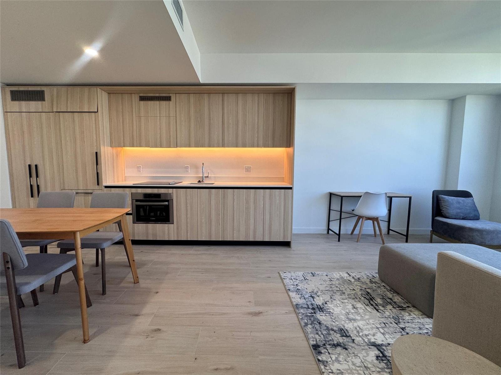 A modern kitchen with light wood cabinetry and integrated appliances sits beside a dining area — 225 N Miami Avenue # 3604, Miami FL 33128, MIAMI, FL