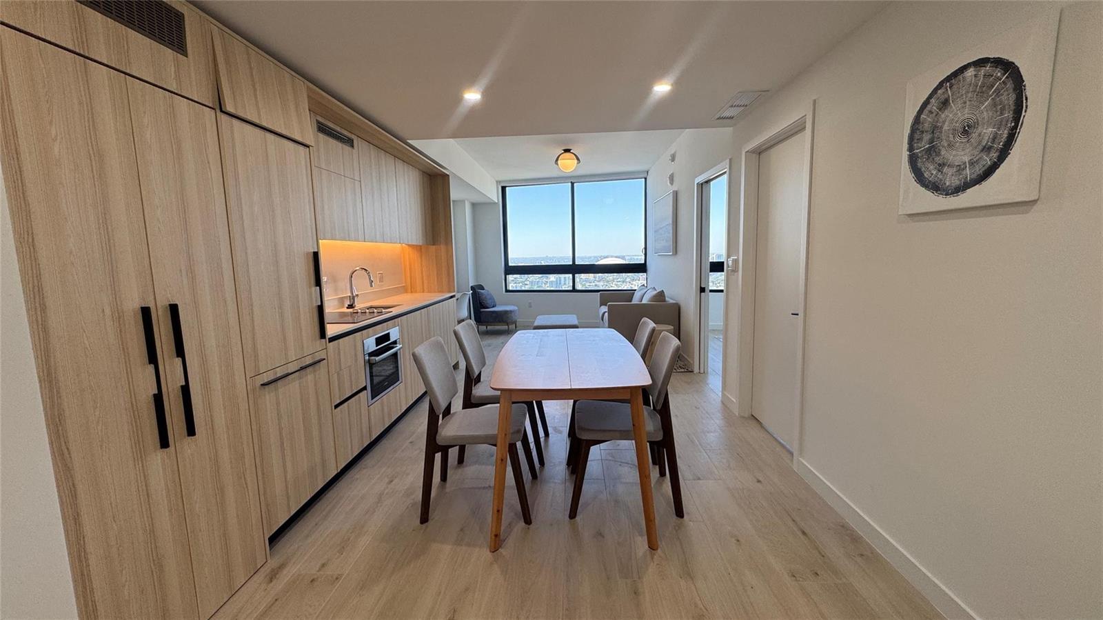 A modern kitchen and dining area features light wood cabinetry, stainless appliances, and city views — 225 N Miami Avenue # 3604, Miami FL 33128, MIAMI, FL