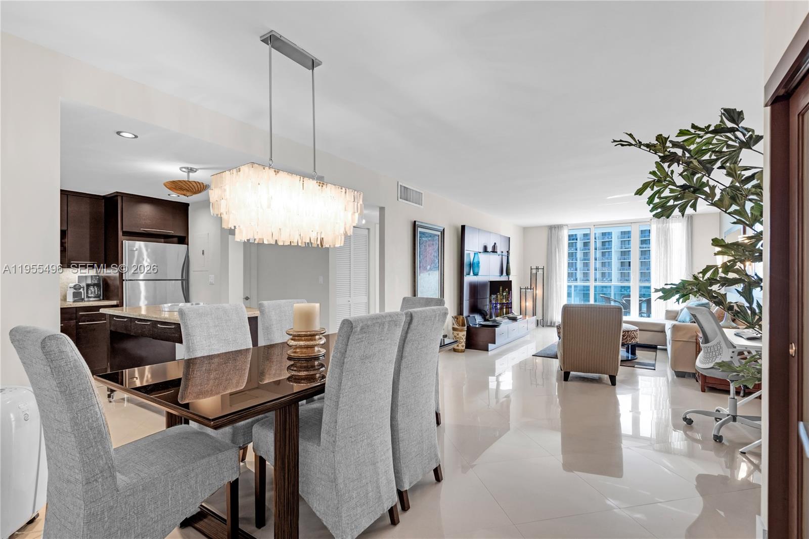A dining area with a chandelier and chairs opens into a living room with tile floors — 2301 Collins Ave # 1006, Miami Beach FL 33139, MIAMI BEACH, FL