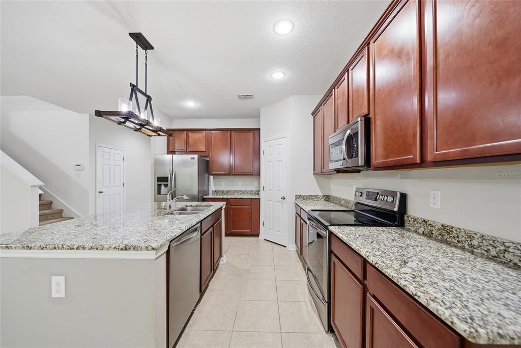A kitchen features dark wood cabinets, granite countertops, stainless steel appliances, and a kitchen island — 30643 WALKER CUP PLACE, WESLEY CHAPEL, FL