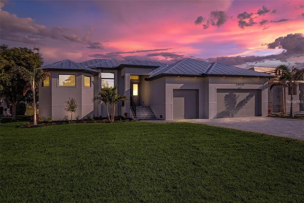 A modern single-story house with a metal roof and a three-car garage at sunset — 24487 GIJON LANE, PUNTA GORDA, FL