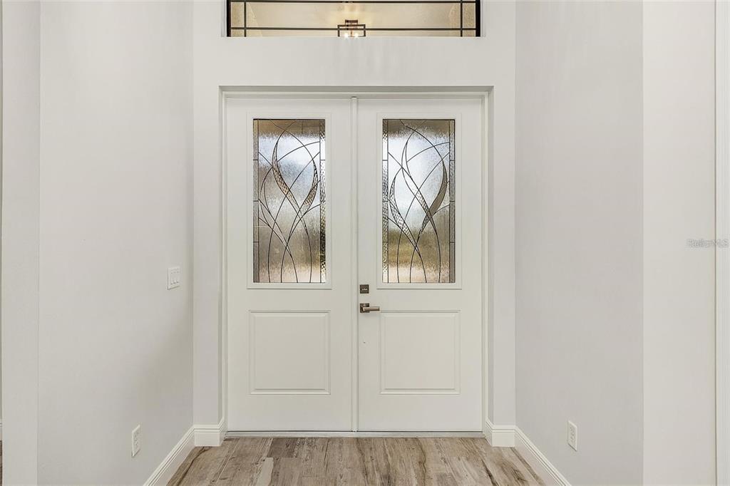 A white double front door with decorative glass panels sits in a bright entryway — 24487 GIJON LANE, PUNTA GORDA, FL