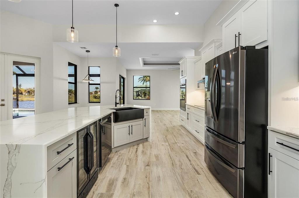 A modern kitchen features white cabinetry, a large marble-topped island, and a black farmhouse sink — 24487 GIJON LANE, PUNTA GORDA, FL