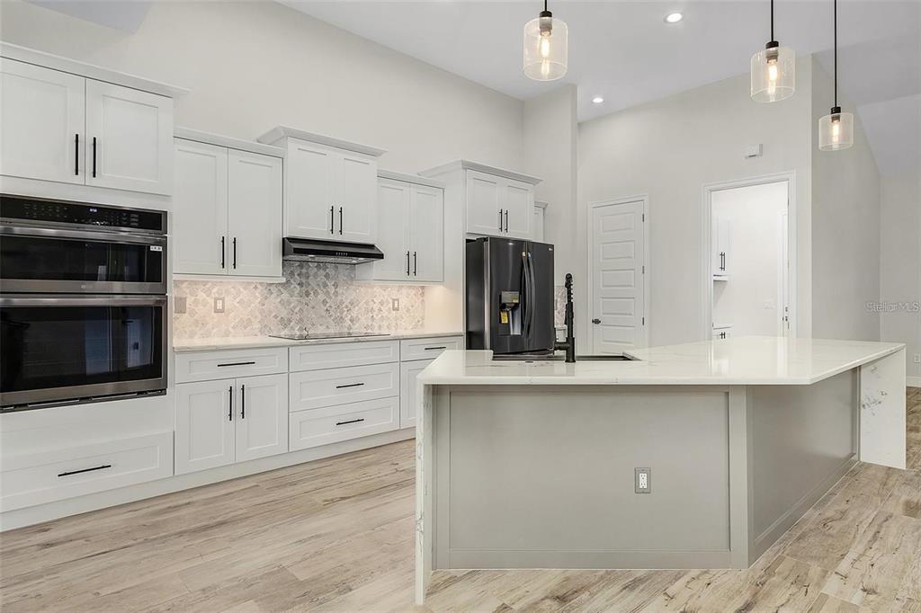 A modern kitchen features white cabinetry, a gray island, stainless steel appliances, and wood-look flooring — 24487 GIJON LANE, PUNTA GORDA, FL