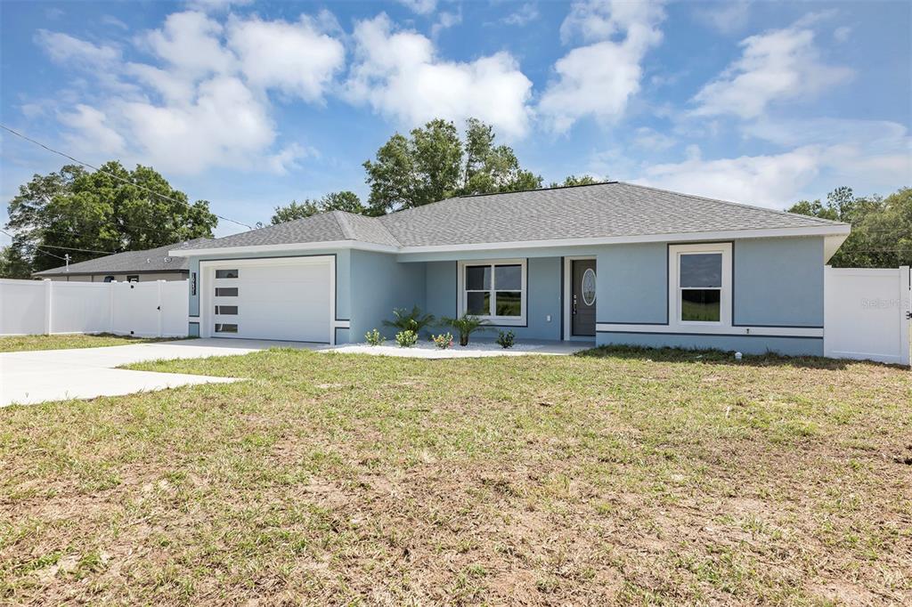 A light blue single-story house with a white garage door and a white vinyl fence — 10431 SW 140TH AVENUE, DUNNELLON, FL