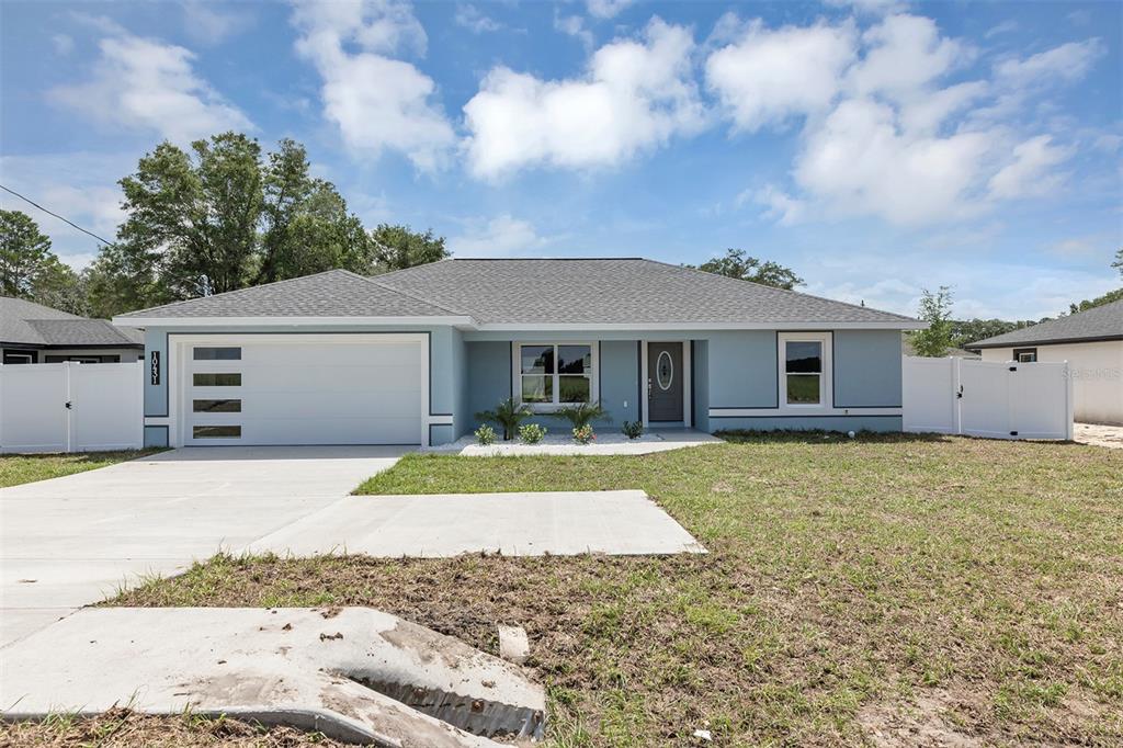 A single-story light blue house with a two-car garage and a white vinyl fence — 10431 SW 140TH AVENUE, DUNNELLON, FL