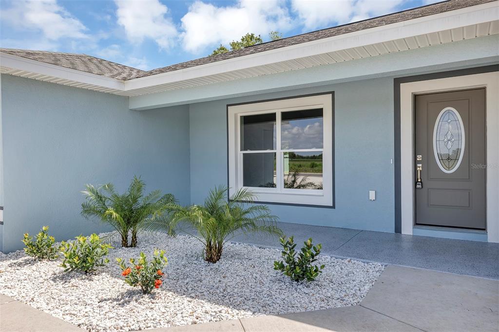 A light blue house exterior features a gray front door and a small rock garden — 10431 SW 140TH AVENUE, DUNNELLON, FL