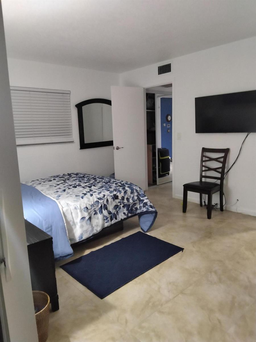 A bedroom with a bed, a chair, a wall-mounted television, and a closet doorway — 399 Brittany # L, Delray Beach FL 33446, DELRAY BEACH, FL