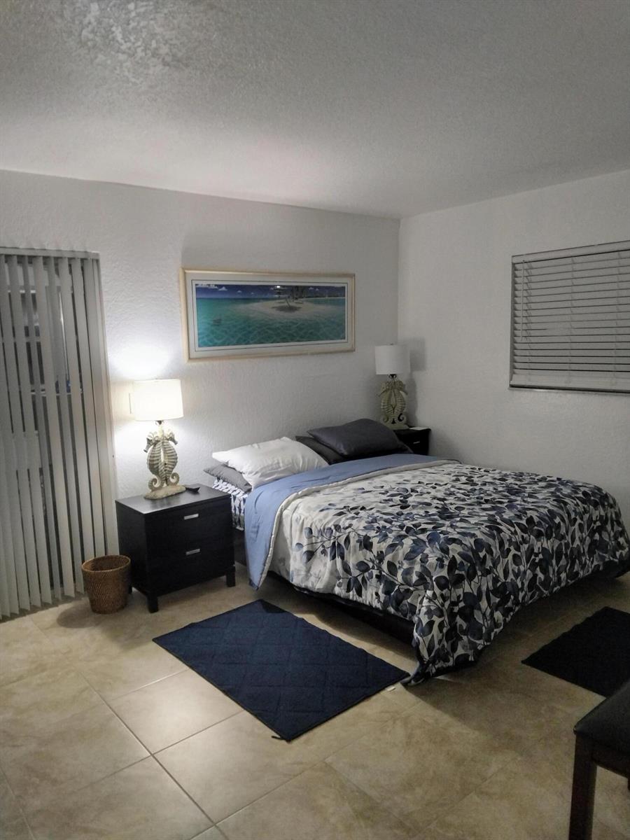 A bedroom features a bed with a floral comforter, two nightstands, and tiled flooring — 399 Brittany # L, Delray Beach FL 33446, DELRAY BEACH, FL
