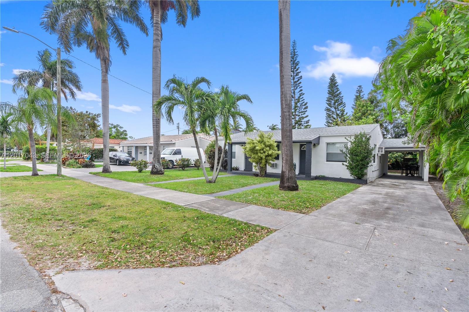 A single-story white house with a concrete driveway and palm trees in the front yard — HALLANDALE BEACH, FL