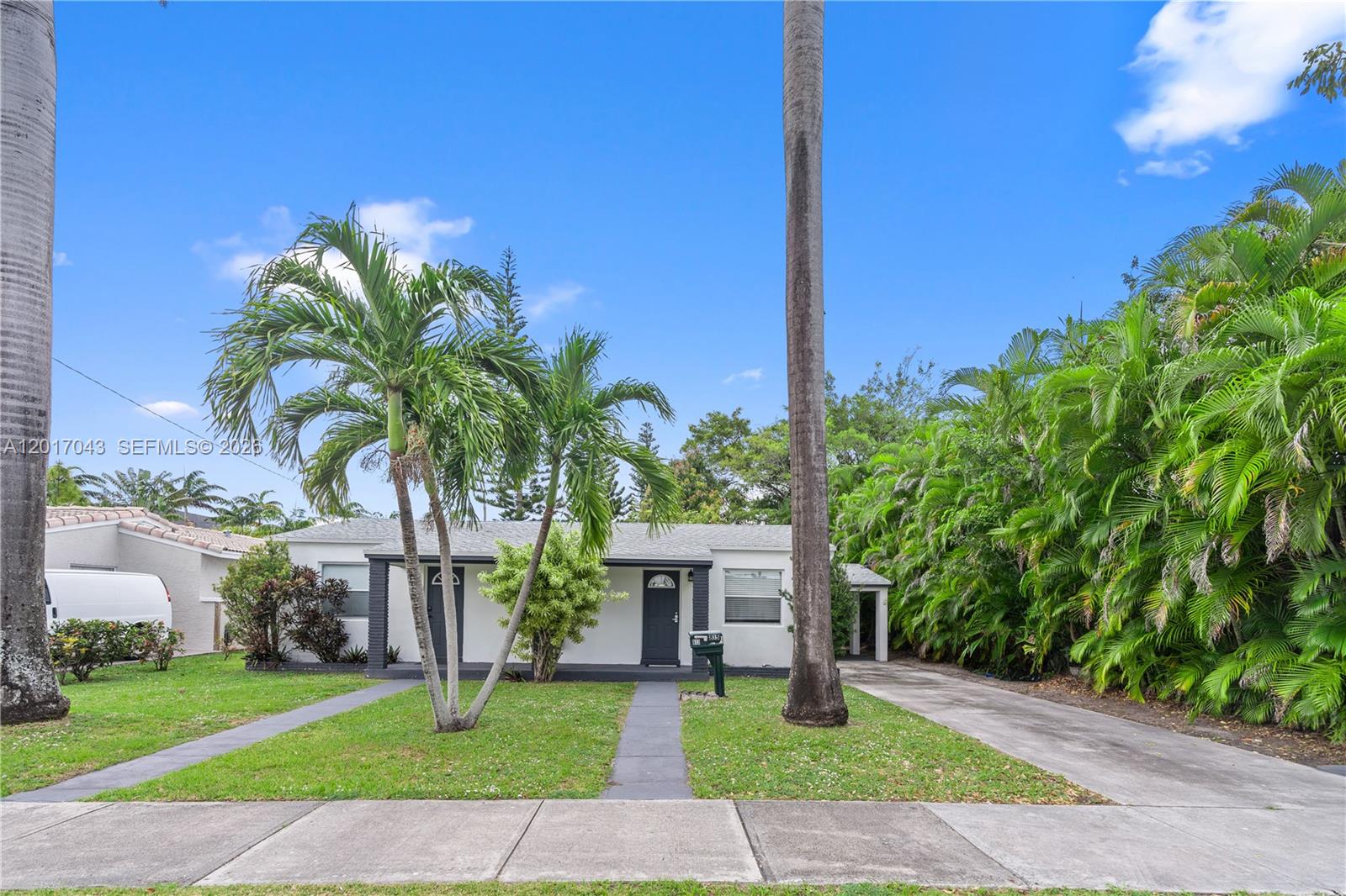 A single-story house with a white exterior, dark trim, and palm trees in the yard — HALLANDALE BEACH, FL