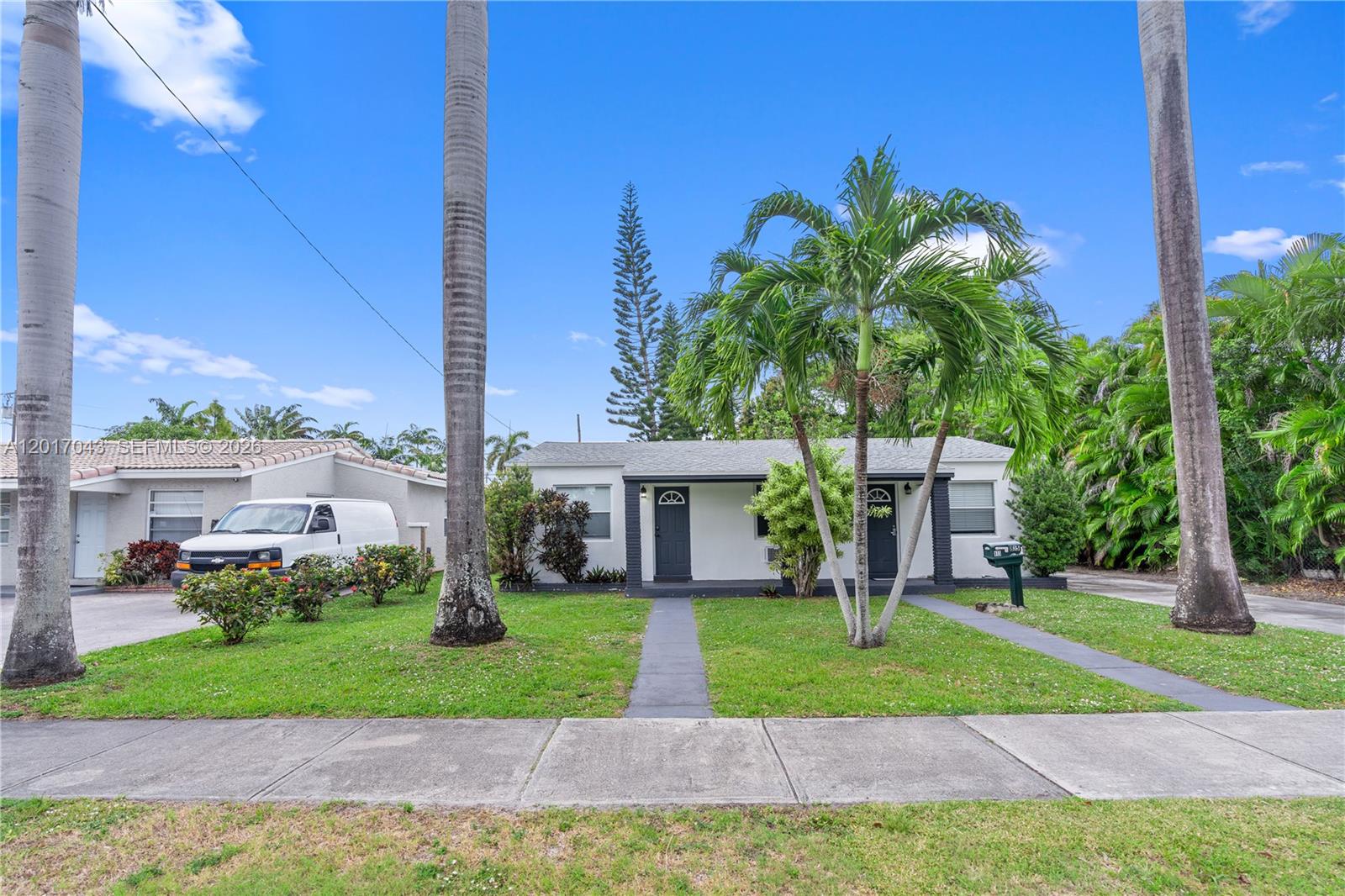 A single-story house with a white exterior, two dark doors, and palm trees in front — HALLANDALE BEACH, FL