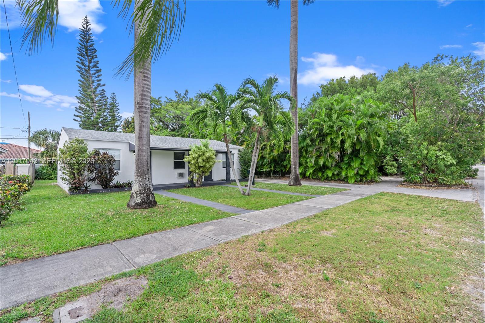 A white single-story house with a lawn, palm trees, and a concrete walkway — HALLANDALE BEACH, FL