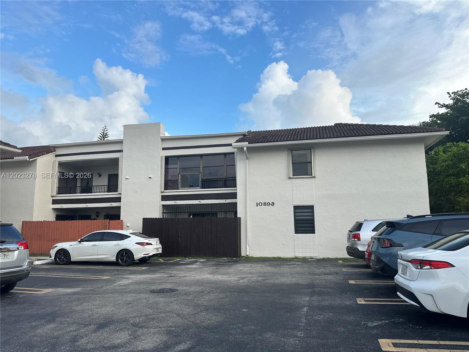 A two-story white stucco apartment building features a parking lot and a wooden privacy fence — 10893 NW 7th St # 27, Miami FL 33172, MIAMI, FL