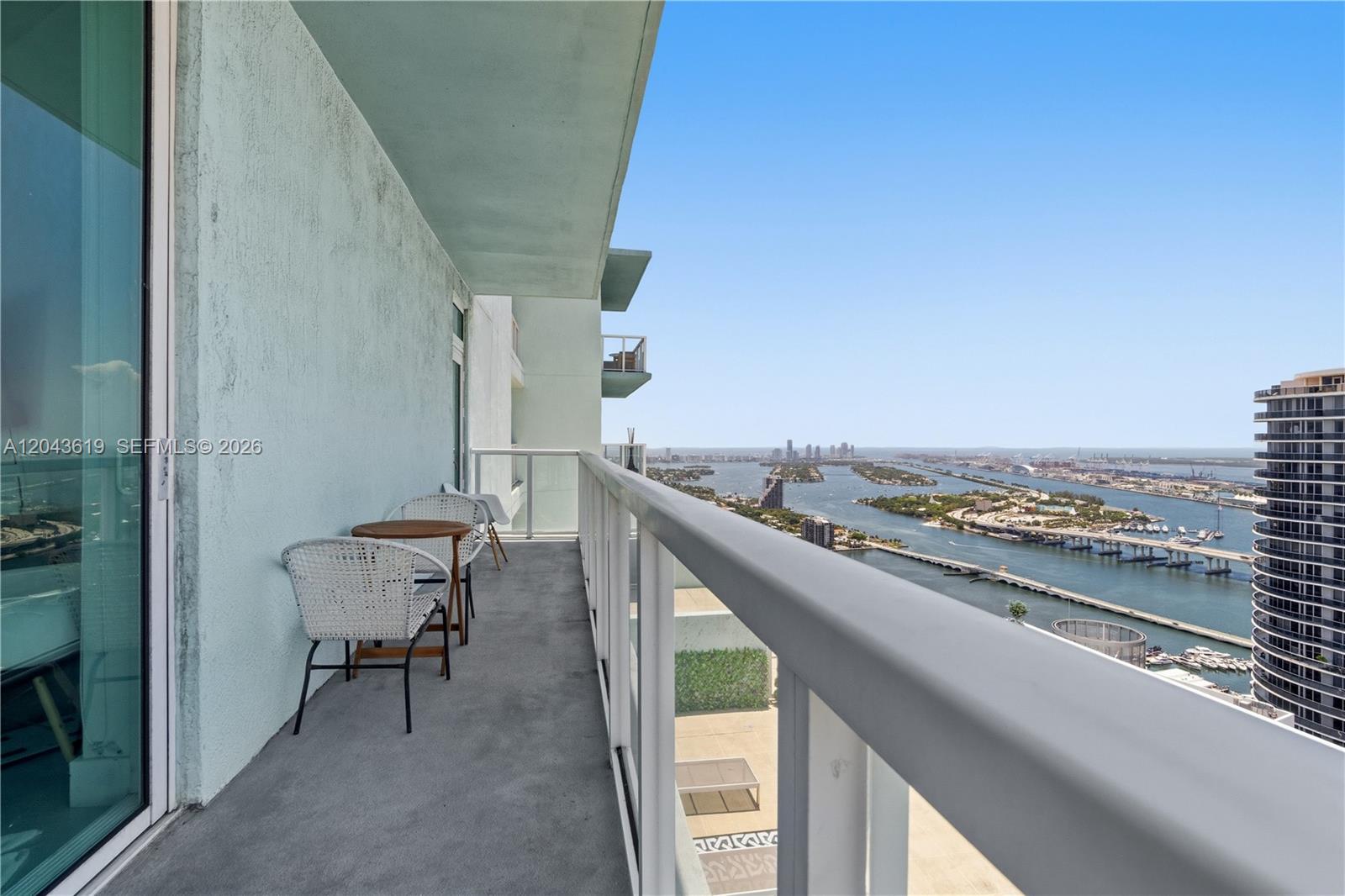 A high-rise balcony features a small table, two chairs, and a panoramic water view — 1900 N Bayshore Dr, Miami FL 33132, MIAMI, FL