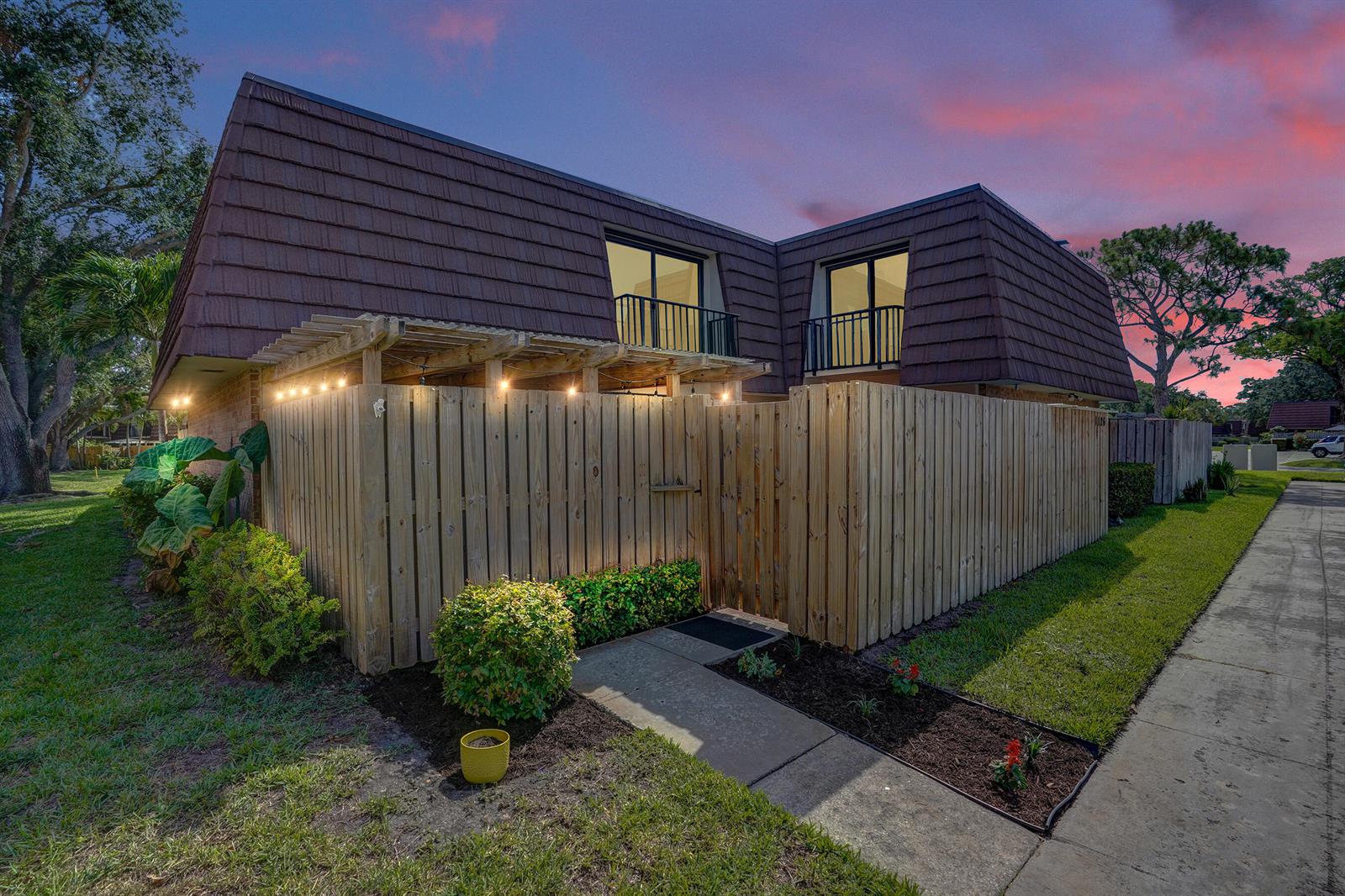 A two-story townhouse exterior with a wooden privacy fence, pergola, and balcony at dusk — 1126 11th Lane, Palm Beach Gardens FL 33418, PALM BEACH GARDENS, FL